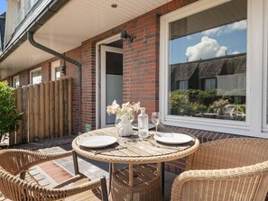 Une terrasse avec des meubles en osier, une table dressée pour deux personnes et un mur en briques.