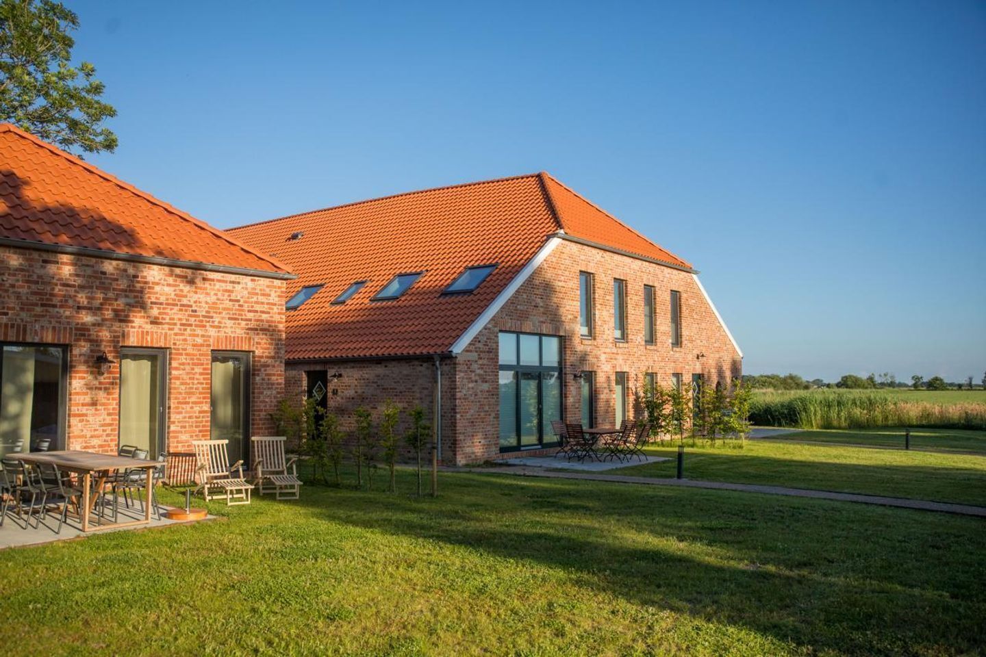 Un bâtiment moderne en briques, doté d’un toit à pente recouvert de tuiles rouges, de grandes fenêtres et d’une pelouse verdoyante.