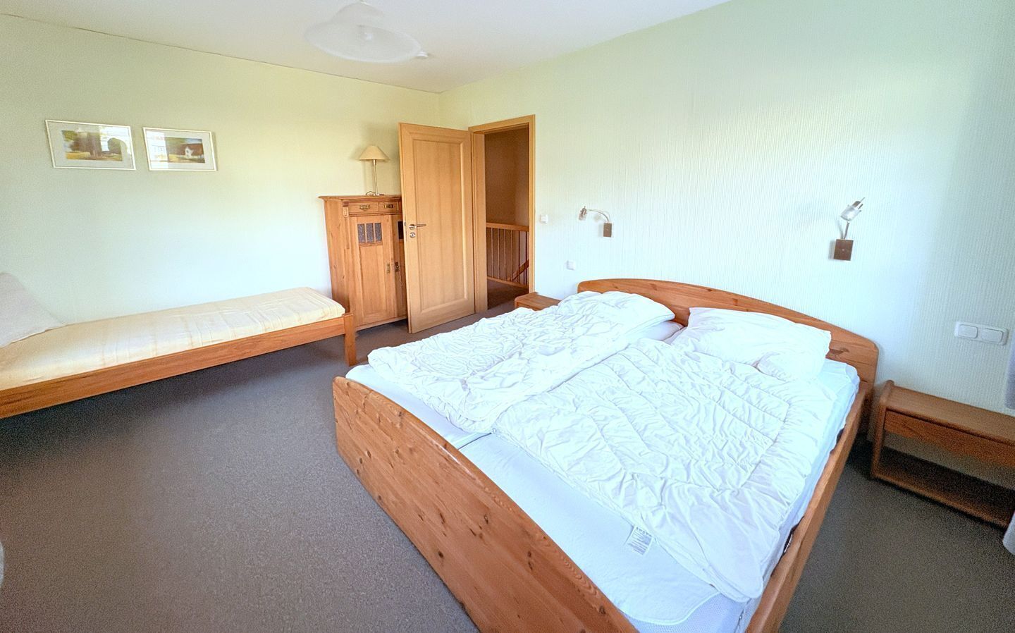 A bedroom with a wooden bed, a wooden bench, a wardrobe, and a door leading to another room.