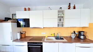 Moderni keittiö, jossa on valkoiset kaapit, sisäänrakennettu uuni, mikroaaltouuni ja kahvinkeitin.