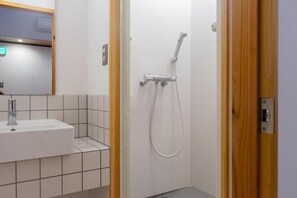 Un baño con lavamanos blanco, paredes con azulejos y ducha con cabezal de ducha manual.