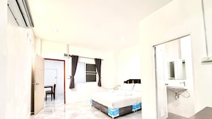 A hotel room with a bed, a desk, a chair, a window with curtains, a mirror, and a bathroom with a sink. - Jasmine Residence (Patong)
