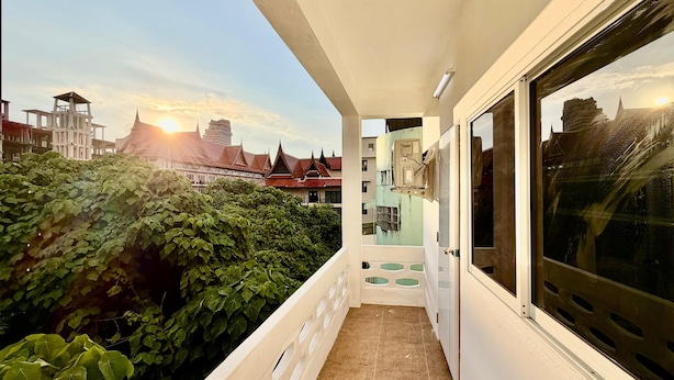 A balcony with a view of a cityscape, including buildings and a sunset. - Jasmine Residence (Patong)