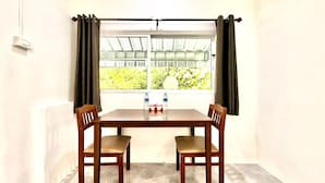A room with a table and two chairs, a window with curtains, and a view of greenery outside. - Jasmine Residence (Patong)