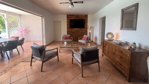 Ein geräumiger Wohnbereich mit Deckenventilator, einem an einer Holzwand befestigten Fernseher, einem Esstisch mit Stühlen und einer Holzkabine.