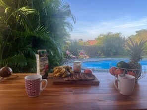 Uma mesa de madeira com uma bebida tropical, pão fatiado e uma abacaxi.