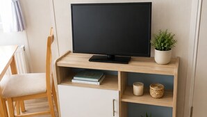 Ein Zimmer mit einem Holztisch, einem Fernseher, einem Sessel und einem Schrank.