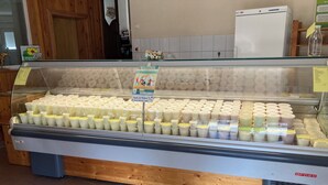 Un expositor con varios productos lácteos, una barra de madera y un refrigerador blanco al fondo.