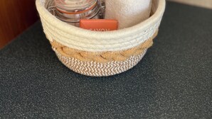 Una cesta tejida con un tarro y una pastilla de jabón sobre una encimera.