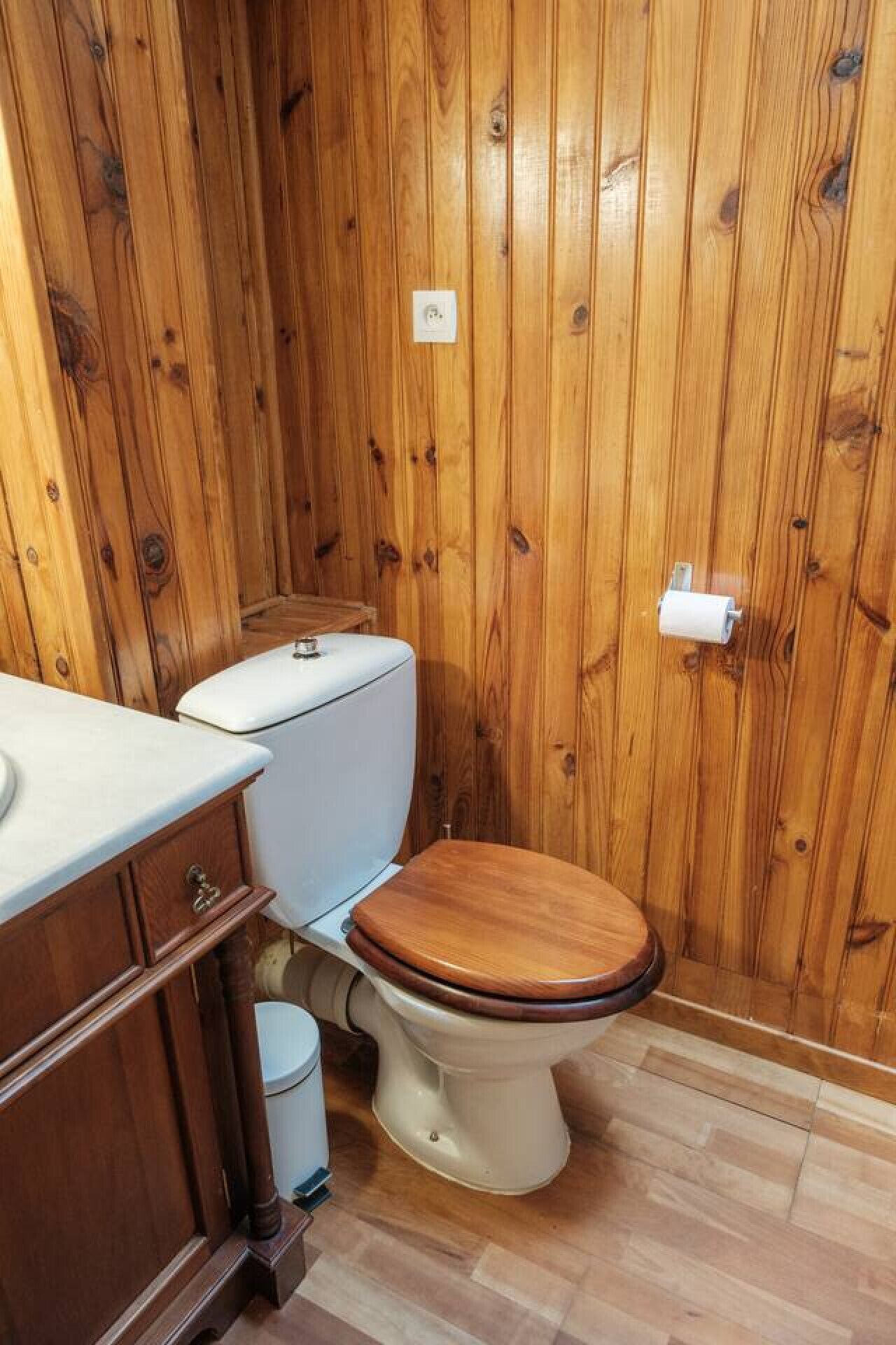 Un baño con paneles de madera, un inodoro, un lavabo y un armario.