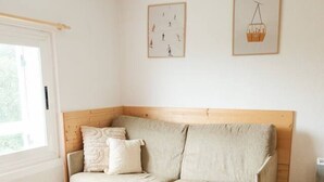 A cozy room with a wooden headboard sofa, a round table with a candle, and a window with a view of greenery. - Studio chaleureux avec vue montagne au cœur de Font-Romeu (Font-Romeu-Odeillo-Via)