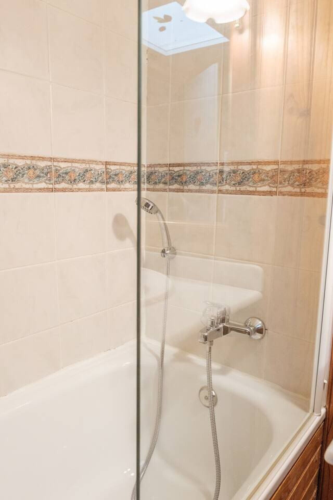 Une douche fermée par des parois en verre, équipée d’un pommeau de douche à main et d’un pommeau de douche fixe.