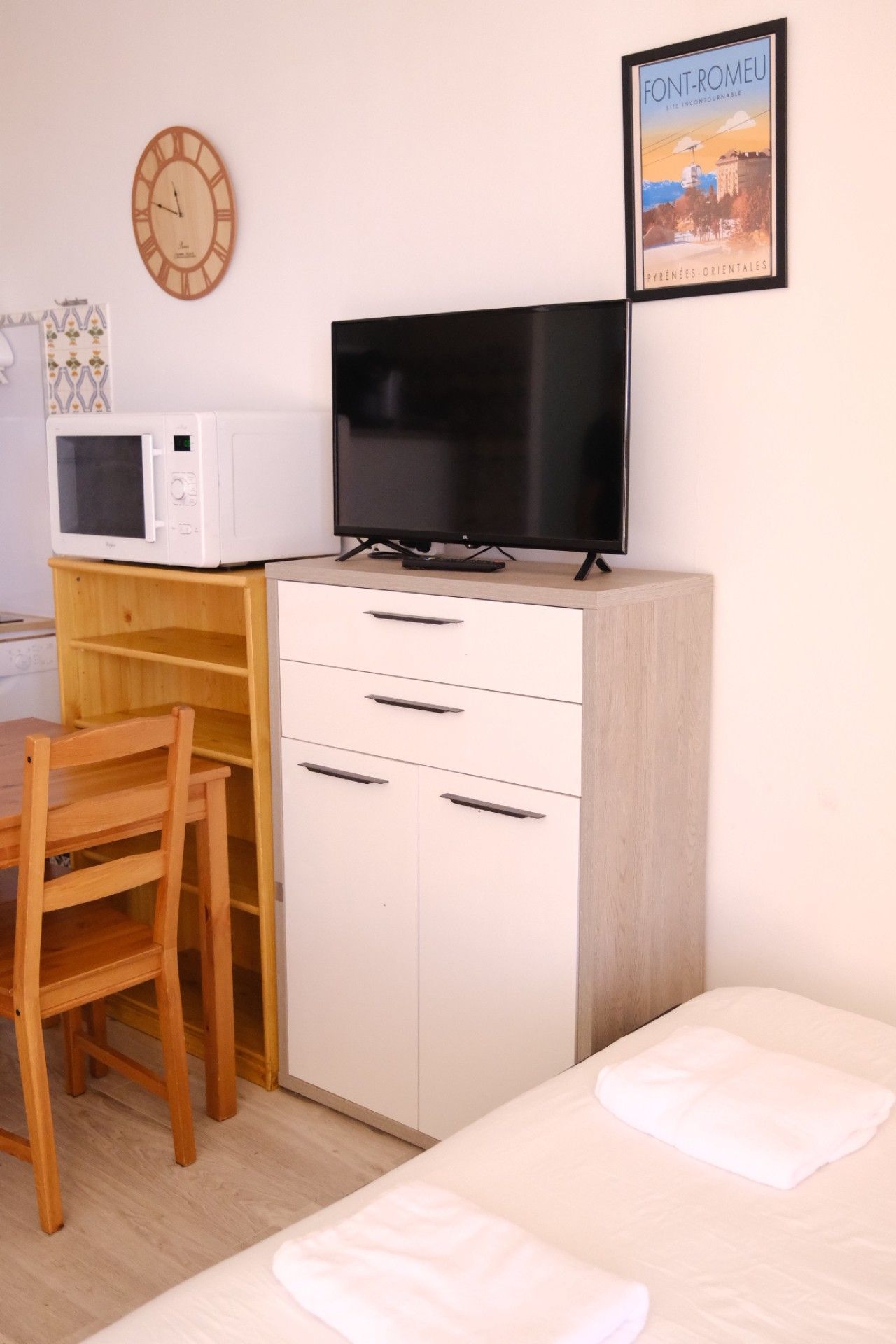 Ein Schlafzimmer mit einem Bett, einem Schreibtisch mit Fernseher, einem Sessel, einer Mikrowelle und einer Wanduhr.