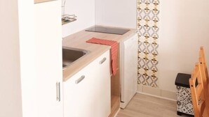 Eine kleine Küche mit weißen Schränken, einem eingebauten Backofen und einer Holzarbeitsplatte. Ein rotes Handtuch hängt am Backofen, und eine Holzstuhls ist in der Ecke zu sehen.