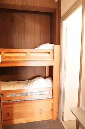 A bunk bed with a wooden frame and a lower drawer, a small bench, and a door leading to another room. - Studio cabine avec balcon ensoleillé pour 6 personnes en hyper-centre (Font-Romeu-Odeillo-Via)