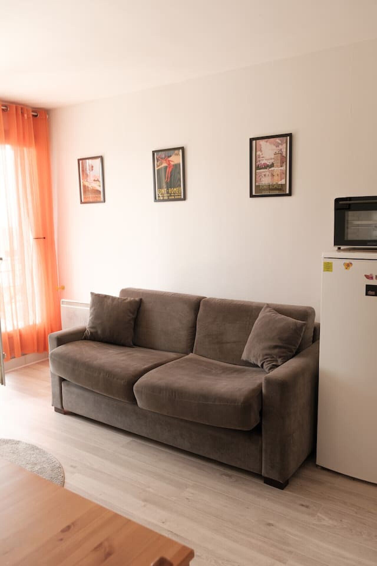 A living room with a brown sofa, a white refrigerator, and two framed pictures on the wall.