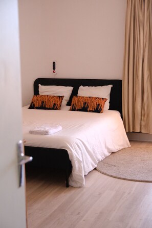 Un dormitorio con cama, almohadas, mesita de noche y puerta.