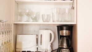 Eine Küche mit einem weißen Kühlschrank, einer Kaffeemaschine, einem Toaster und verschiedenen Gläsern in Regalen.