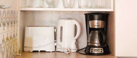 A kitchen with a white refrigerator, a coffee maker, a toaster, and various glassware on shelves.