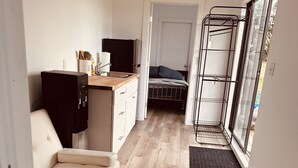 Ett kompakt bostadsutrymme med ett litet kök, en soffa, en säng och en glasdörr som leder ut till en balkong.
