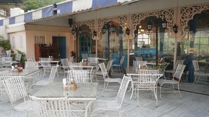 An outdoor patio with white metal chairs and tables, decorative arches, and hanging lanterns. - Hotel Amer Fort (Amer)