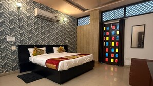 A modern bedroom with a large bed, a ceiling fan, an air conditioning unit, and a view through a door with colorful glass panels. - Hotel Amer Fort (Amer)