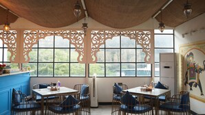A dining area with a high ceiling, large windows with decorative screens, and a mural on the wall. - Hotel Amer Fort (Amer)