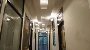 A hallway with recessed lighting, framed artwork on the walls, and a large window at the end. - Hotel Amer Fort (Amer)