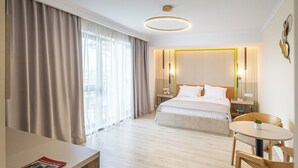 A hotel room with a bed, bedside tables, a desk, a chair, and a round table.