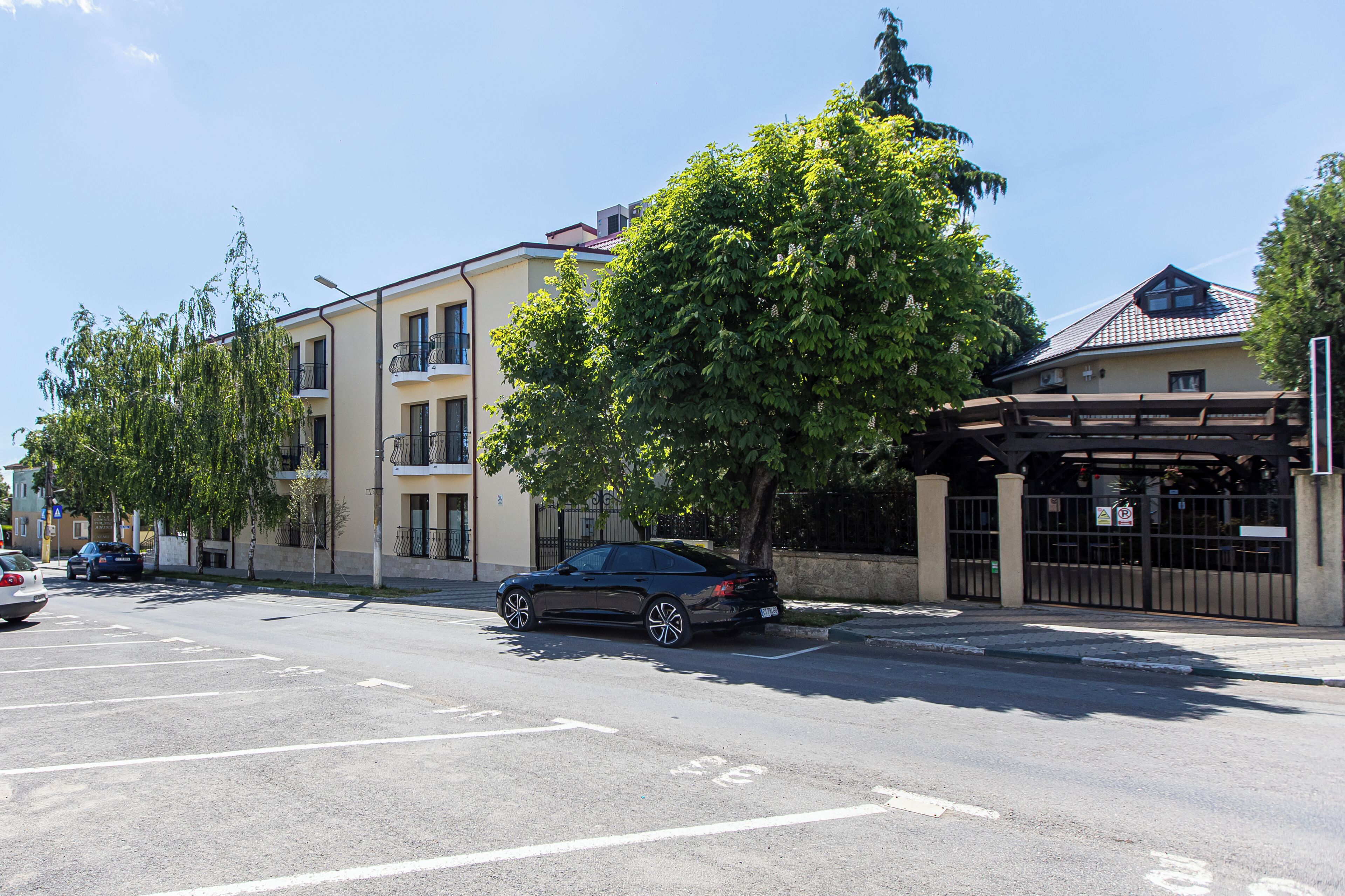 A multi-story building with balconies, a parking lot, and a tree in front.