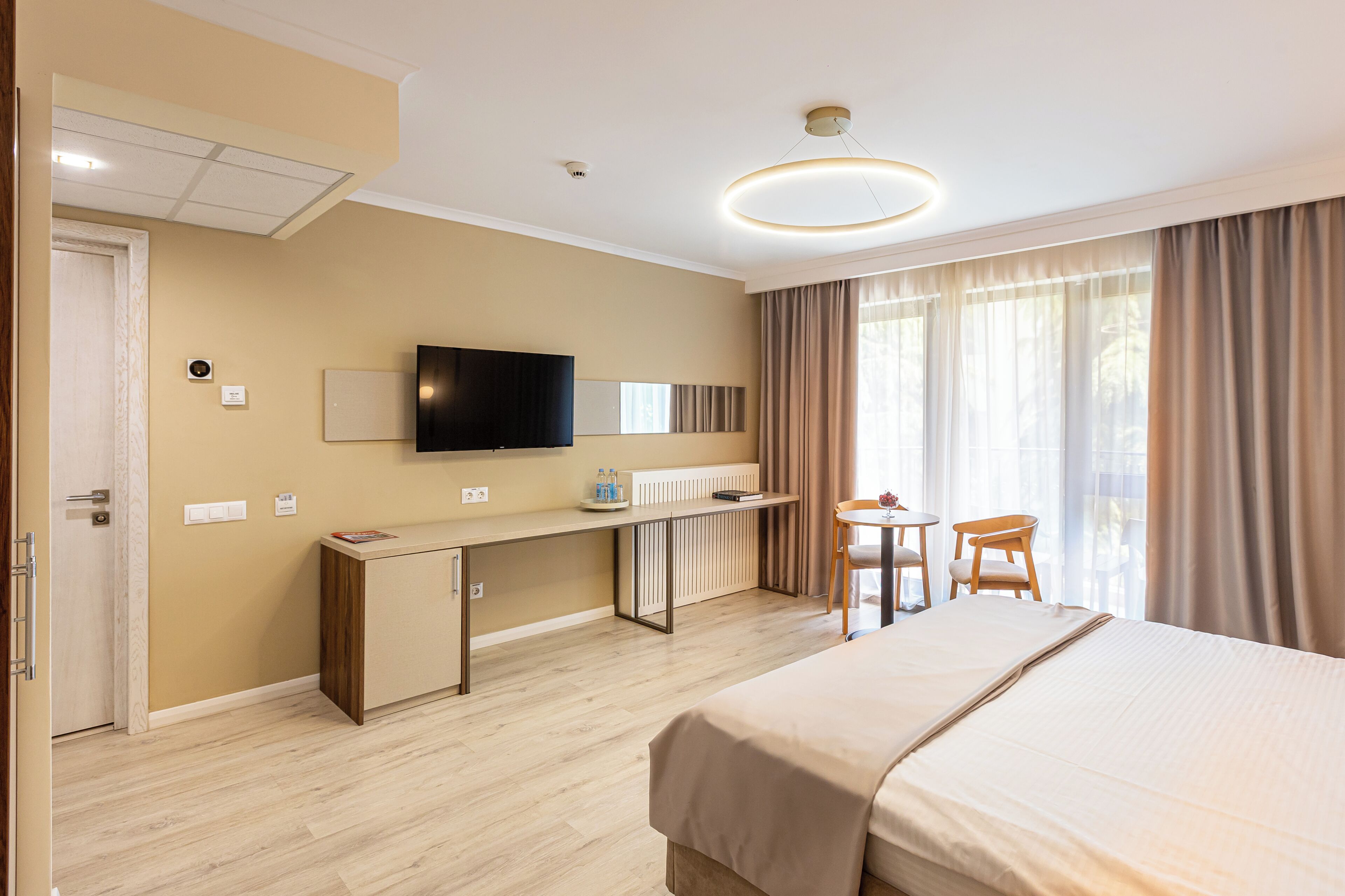 Una camera d'albergo con un letto, una scrivania, una sedia, TV e ampie finestre.