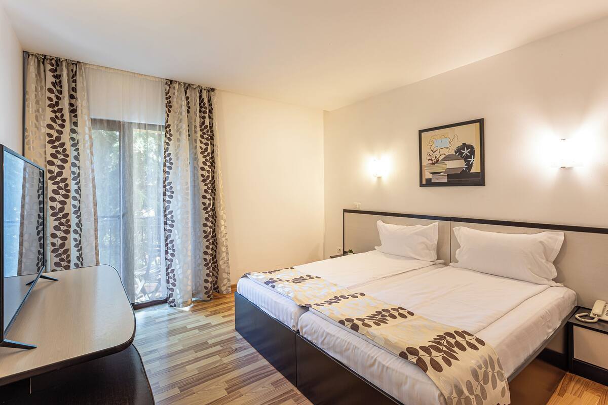 A hotel room with a bed, a desk, a chair, a phone, and a painting on the wall.