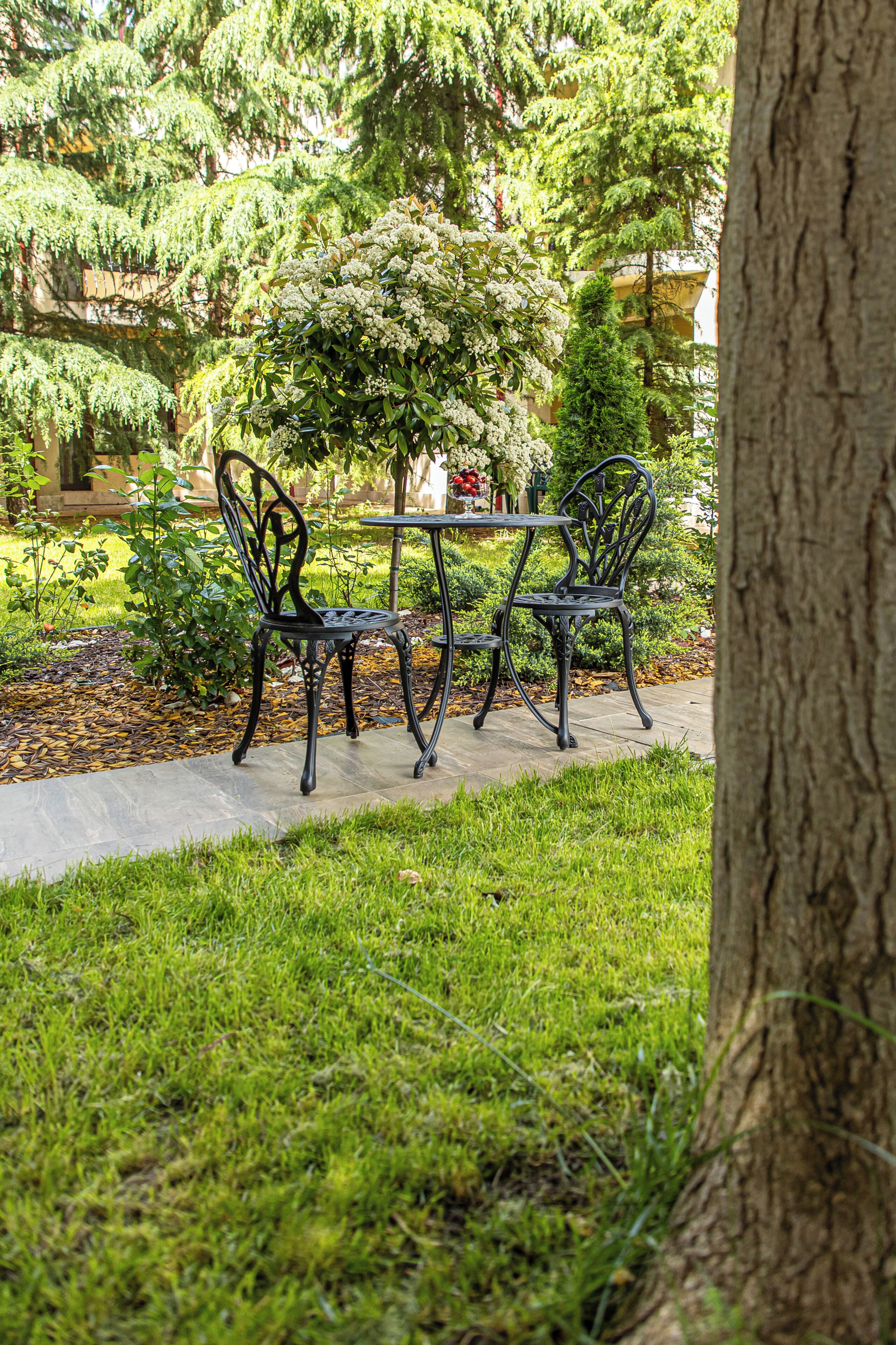 A patio with a table and chairs, surrounded by greenery and a tree.