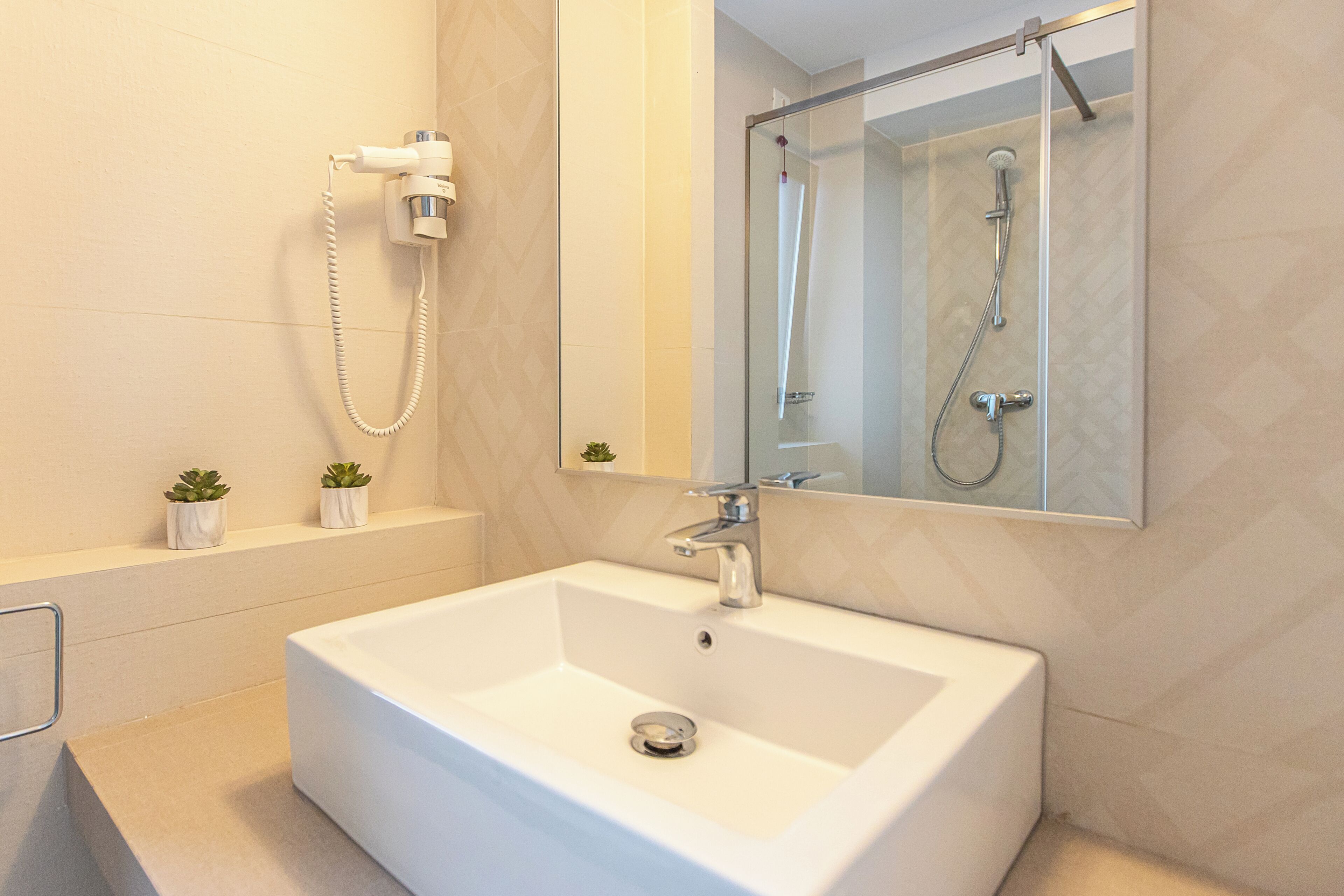 Une salle de bain moderne avec un grand lavabo blanc, une douchette à main et un miroir au-dessus du lavabo.