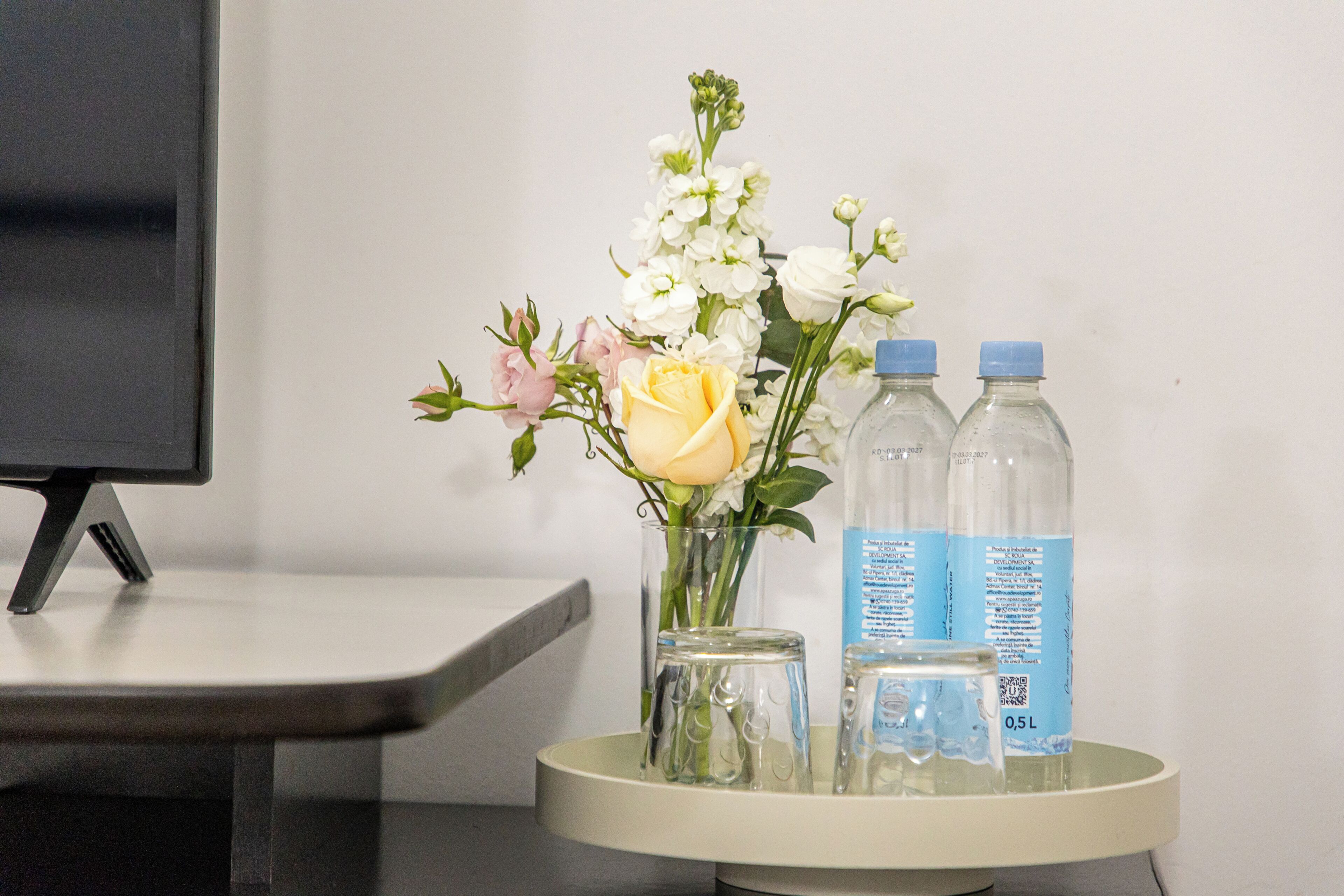 A table with a vase of flowers, two water bottles, and a glass.
