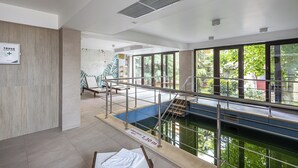 An indoor swimming pool with a clear view of the outside, a sign indicating a 7.30m depth, and a wooden wall on the left.