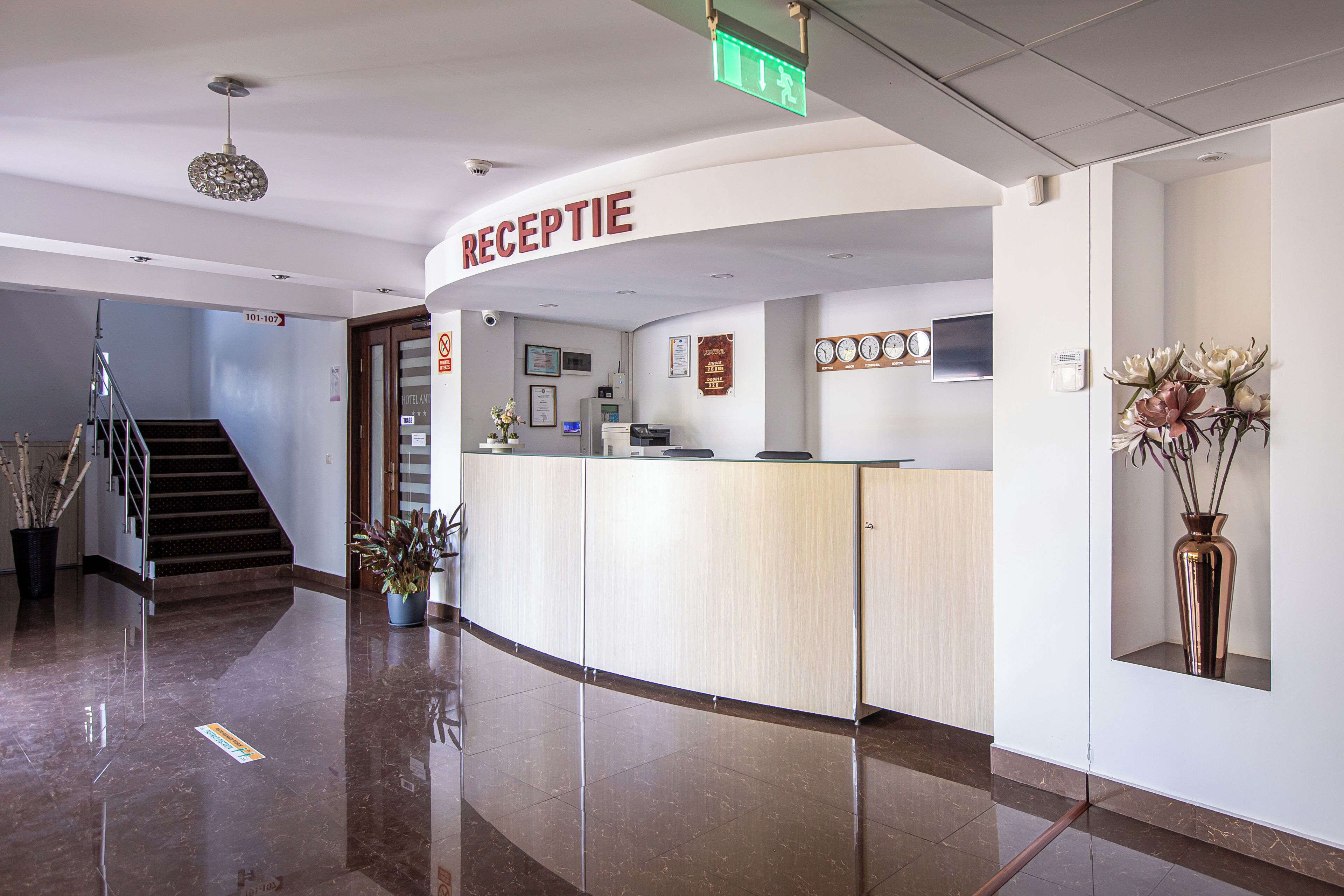 A hotel reception area with a reception desk, a staircase, and a potted plant.