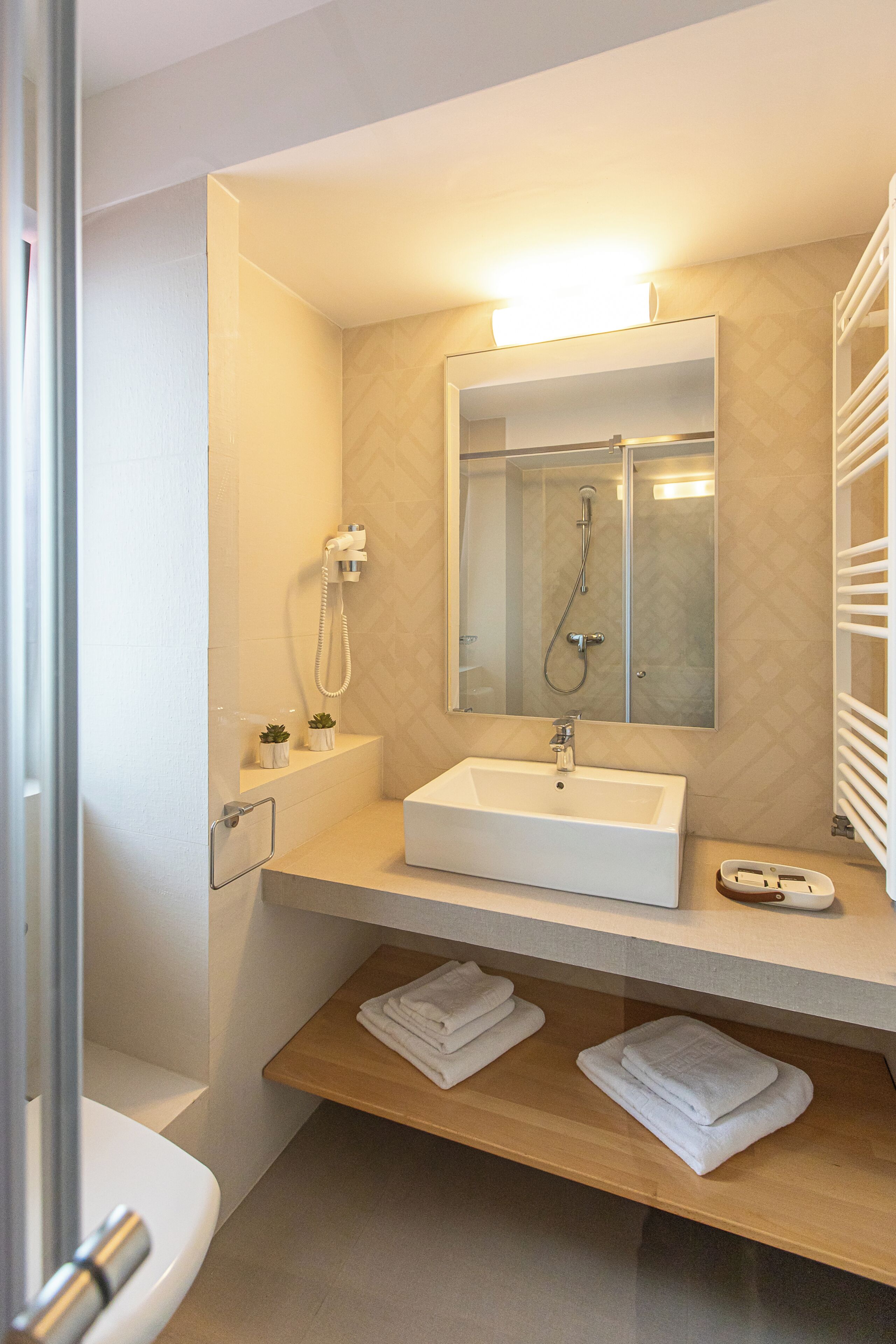 A bathroom with a white sink, a mirror, a shower, and a towel rack.