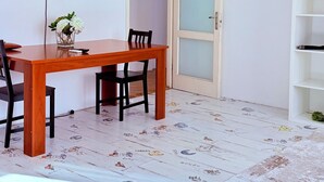 Et spiseområde med et træbord og stole, et fjernsyn ophængt på væggen og en dør med sandblæste glaspaneler.