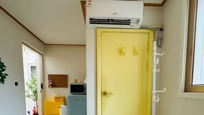 A hallway with a yellow door, a white air conditioning unit above it, and a small plant on the left. - BANANA_Marvelous 1-bedroom studio with AC in EWha Univ. (Seodaemun-gu,)