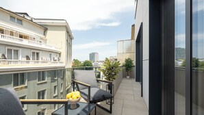 A modern balcony with a glass railing, a small table with a bowl of fruit, and two grey chairs. - Manu Art Living (Bucharest)