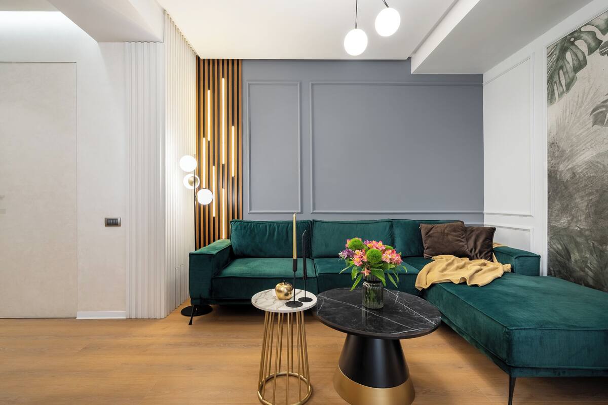 Un salón moderno con un sofá verde, una mesa redonda negra y una mesita auxiliar con un jarrón de flores.