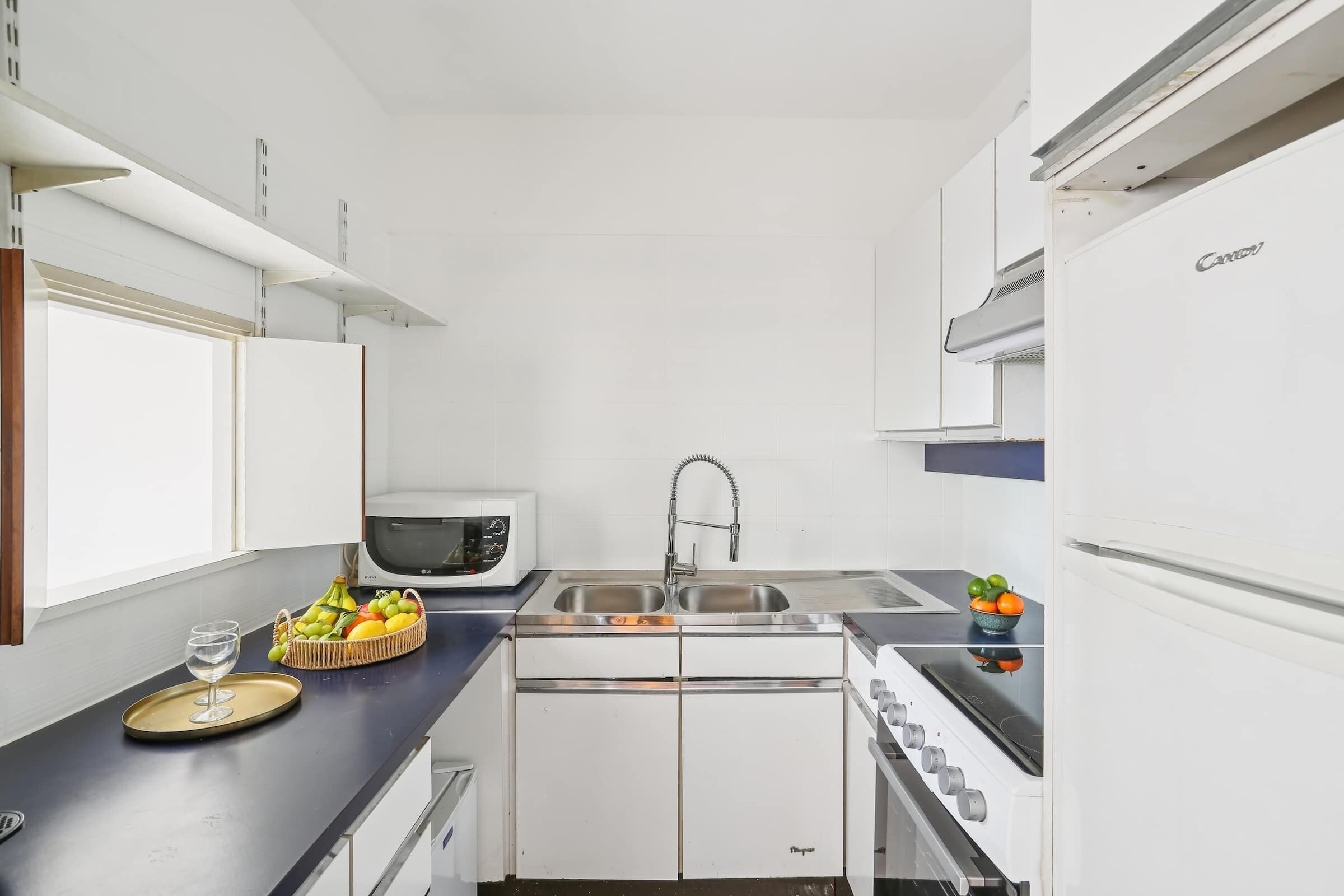 Une cuisine de taille réduite, avec des meubles blancs, un four à micro-ondes, un évier et une cuisinière.