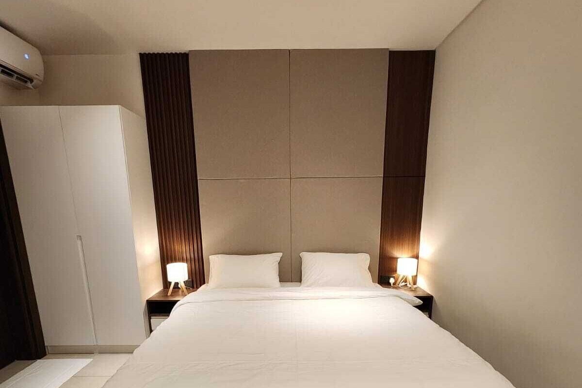 Une chambre d’hôtel moderne avec un grand lit, deux tables de chevet avec lampes, une armoire et un climatiseur au plafond.
