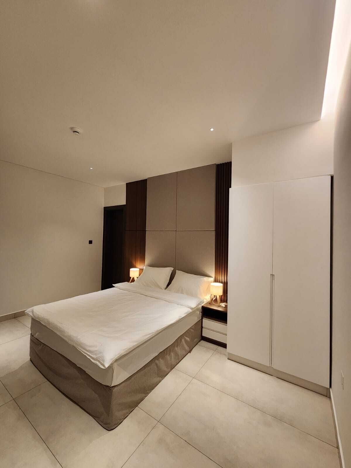 Un dormitorio moderno con una cama grande, lámparas de noche, un armario y una luz en el techo.