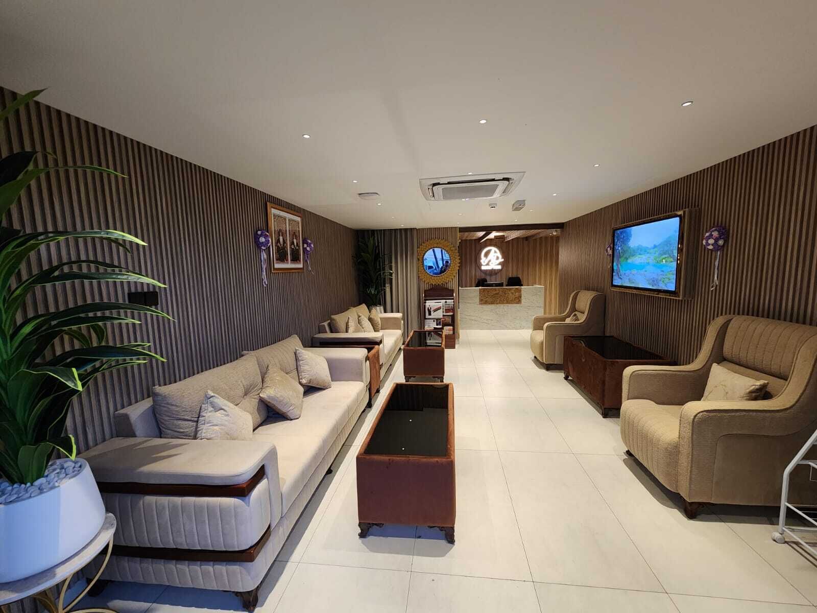 Een moderne hotel lobby met een receptiebalie, zithoek en een groot televisiescherm.