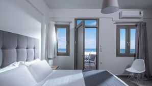 Ett hotellrum med en stor säng, utsikt över havet genom öppna dörrar, en balkong med ett bord och en stol samt en luftkonditioneringsanläggning på väggen.