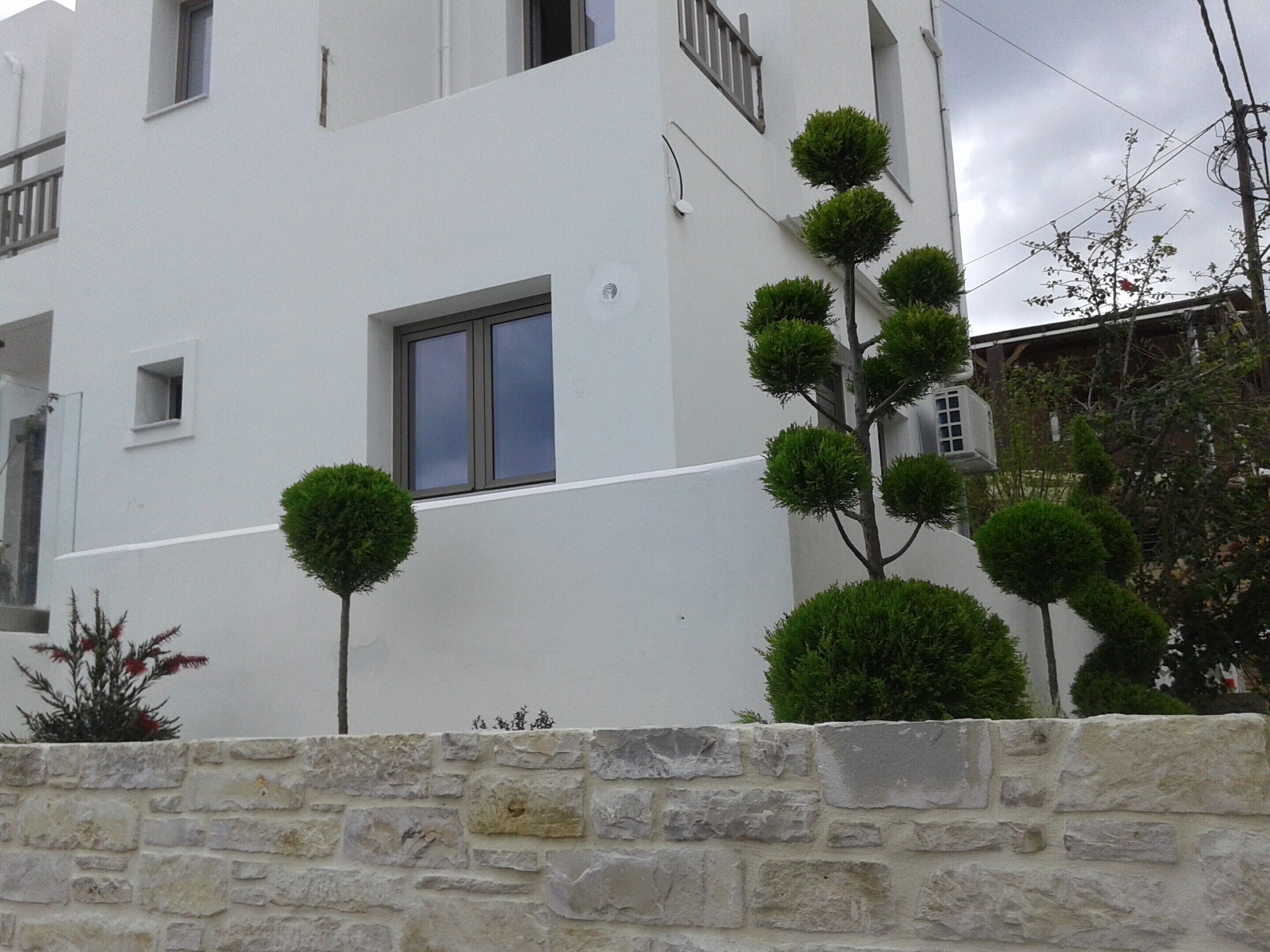 Un edificio moderno con un muro de piedra, una ventana con persianas y un pequeño árbol.