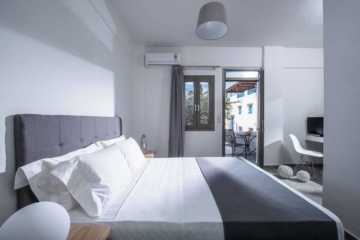 A modern hotel room with a large bed, a desk, and a view of the outside.