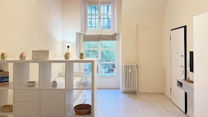 A bright, modern room with a white color scheme, a red ceiling, a large window, a radiator, and a white cabinet with a mirror. - Loft Portici by Piazza Vittorio (Torino)
